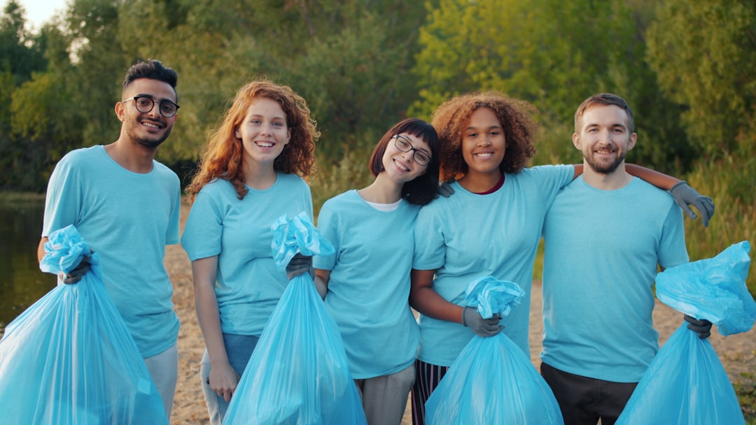 Joyful friends eco activists men and women are holding garbage bags standing on river bank hugging looking at camera. Volunteering and lifestyle concept.